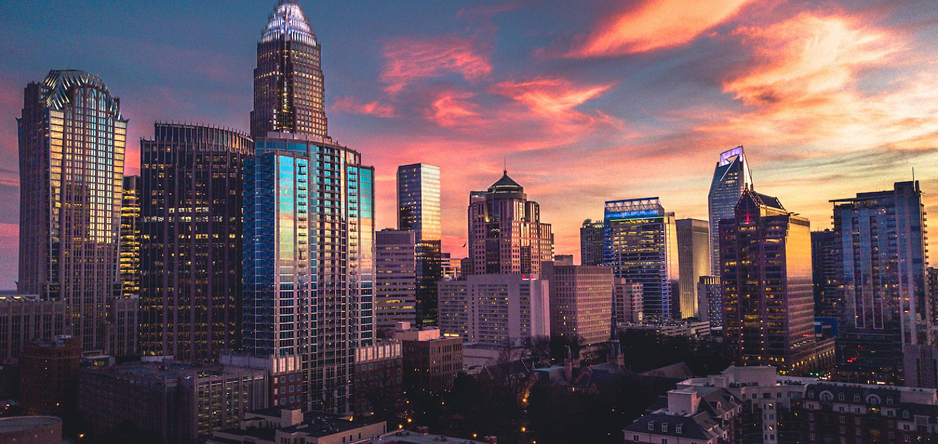 Uptown Charlotte's towers at dusk under a pink and orange sky, the Bank of America Corporate Center at left
